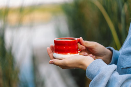 Woman holds cup of coffee on wooden pier on lake