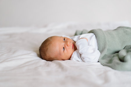 A newborn baby rests on a bed, wrapped in a soft blanket.