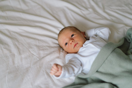 A newborn baby rests on a bed, wrapped in a soft blanket.