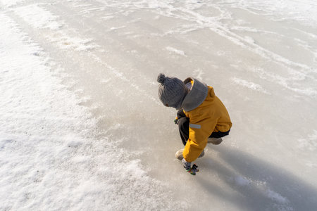 Child having fun in the snow, wearing winter clothing in snowy landscape during daytime.の写真素材