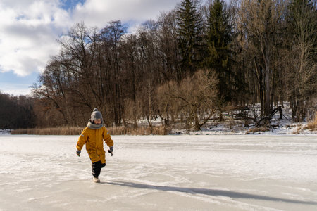 Child having fun in the snow, wearing winter clothing in snowy landscape during daytime.の写真素材