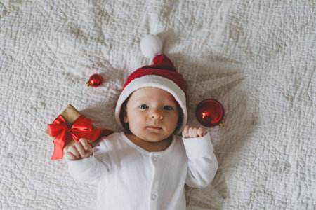 Cute baby in Santa hat with holiday decorations and gifts during Christmas season