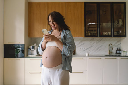 Expecting mother using smartphone in modern kitchen during pregnancyの写真素材