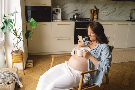 Expecting mother using smartphone in modern kitchen during pregnancyの写真素材