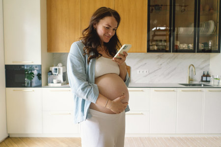 Expecting mother using smartphone in modern kitchen during pregnancy