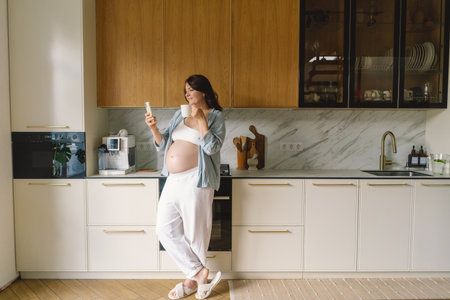 Expecting mother using smartphone in modern kitchen during pregnancyの写真素材