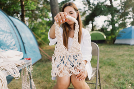 Woman knits bag using macrame technique outdoors near tents. Outdoor hobbies.の写真素材