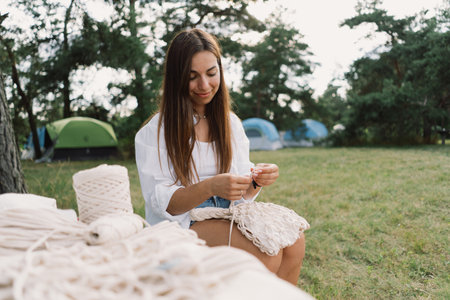 Woman knits bag using macrame technique outdoors near tents. Outdoor hobbies.の写真素材