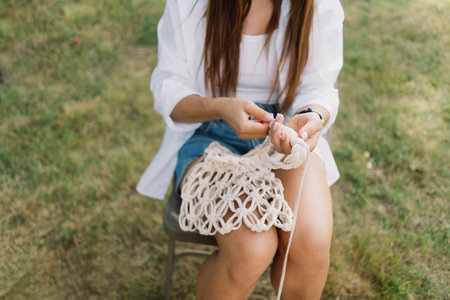Woman knits bag using macrame technique outdoors near tents. Outdoor hobbies.の写真素材