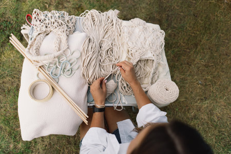 Woman knits bag using macrame technique outdoors near tents. Outdoor hobbies.