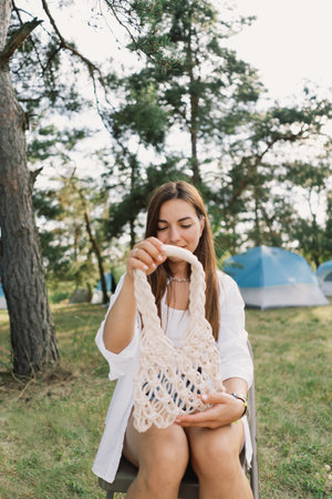 Woman knits bag using macrame technique outdoors near tents. Outdoor hobbies.の写真素材