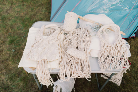Woman knits bag using macrame technique outdoors near tents. Outdoor hobbies.