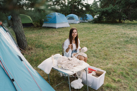 Woman knits bag using macrame technique outdoors near tents. Outdoor hobbies.の写真素材