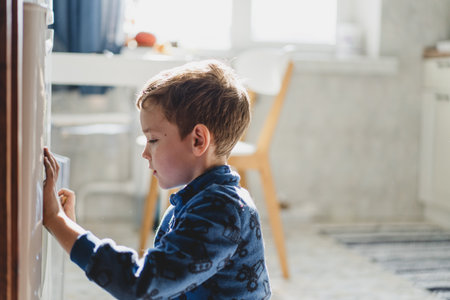 A young boy drawing on the refrigerator with a markerの写真素材
