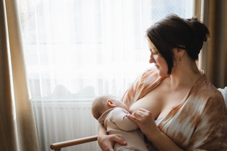 Woman comfortably breastfeeding her baby in a cozy roomの写真素材