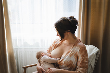 Woman comfortably breastfeeding her baby in a cozy roomの写真素材