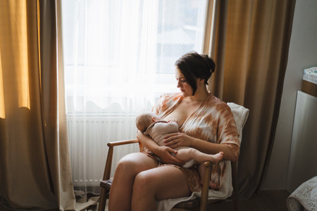 Woman comfortably breastfeeding her baby in a cozy roomの写真素材