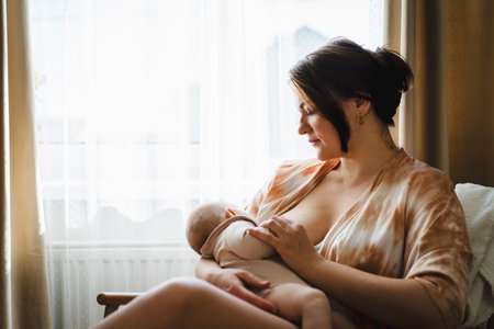 Woman comfortably breastfeeding her baby in a cozy roomの写真素材