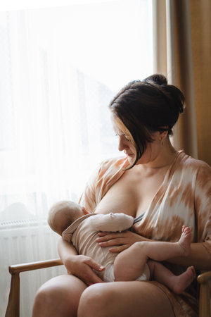 Woman comfortably breastfeeding her baby in a cozy roomの写真素材