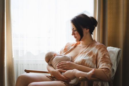 Woman comfortably breastfeeding her baby in a cozy roomの写真素材