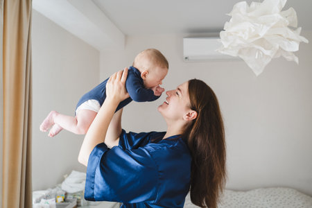 Mother joyfully holds her baby in a bright, cozy room during a joyful morning momentの写真素材
