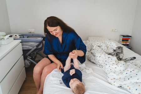 Mother cares for her baby in a cozy bedroom setting during the morning hoursの写真素材