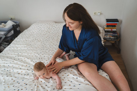 Mother plays with her baby on the bed in a cozy room during morning hours, enjoying precious bonding time togetherの写真素材