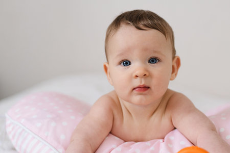 A baby lies on a soft pillow, reaching for a colorful toy.の写真素材