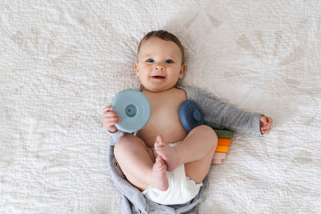 Baby on a soft light blanket and playing with a colorful stacking ring toy.