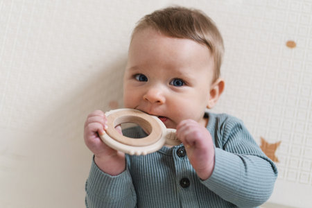 Portrait of a cute baby holding and chewing a wooden teething toy