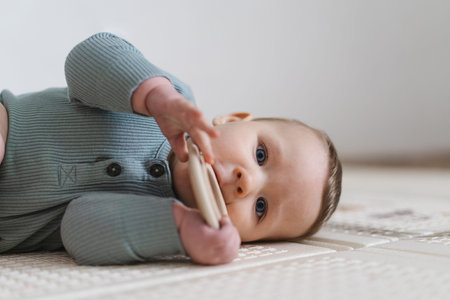 Portrait of a cute baby holding and chewing a wooden teething toy