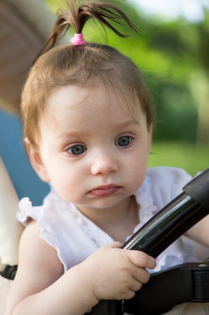 A small child or a girl with a ponytail, a white baby or a toddler with plump lips sits in a...