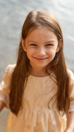 Beautiful, sweet girl or child with long loose hair in beige dress smiling and looking at camera.の写真素材