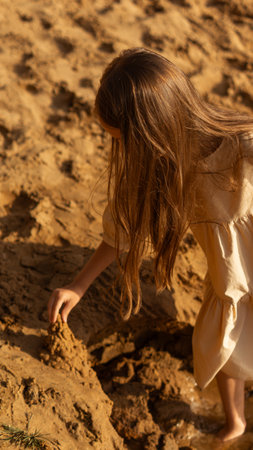 Girl or child at sunset building a sand castle or tower on the seashore or riverside, or playing with sand on a golden sandy beachの写真素材