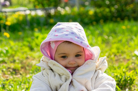 Little child or girl or toddler in jacket and hoodie against blurred green plants smilingの写真素材