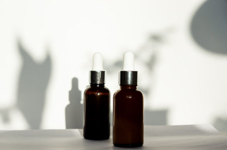 Two brown dropper bottles or glass cosmetic jars without label on white background, front view, close-up. Natural sunlight lightingの写真素材