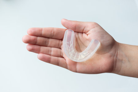A mouth guard for bite alignment or teeth whitening lies on a person's palm. Top view, close-up, on...