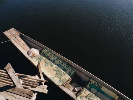 Traditional style wooden boat with straw hat and rugs in it in sunshine. Inle lake, Myanmar.