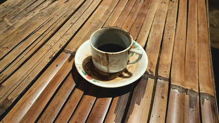 A cup of delicious hot black Indonesian coffee with lots of dregs. Served in a unique, classic and old-fashioned cup on a small plate. Hot coffee on a bamboo table.の写真素材