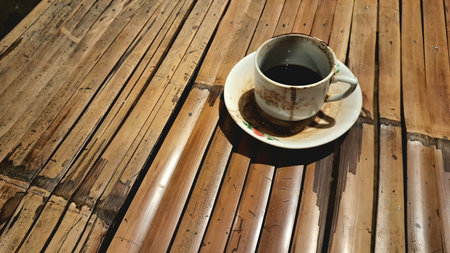 A cup of delicious hot black Indonesian coffee with lots of dregs. Served in a unique, classic and old-fashioned cup on a small plate. Hot coffee on a bamboo table.の写真素材
