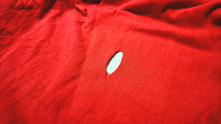 Close Up of Red Cloth with Small Hole Symbolizing Imperfection, Damage, and Textile Tear Conceptの写真素材