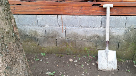 Realistic Dirty Metal Shovel Against Gray Cinder Block Wall and Natural Ground for Infrastructure Development and Manual Construction Work Conceptの写真素材
