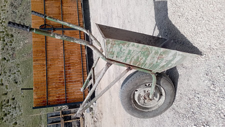 a dirty construction wheelbarrow stands against a wall in the sun, with a construction site in the backgroundの写真素材
