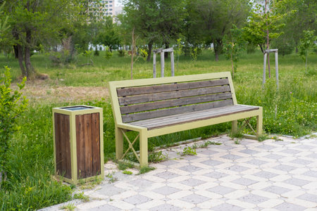 A sturdy wooden bench positioned conveniently alongside a trash can, ideal for outdoor settings and...