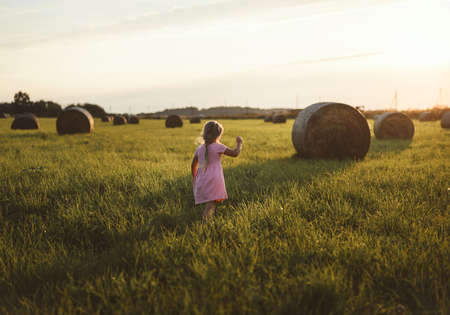 A happy child runs through a field of haystacks at sunsetの写真素材