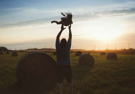 A happy child runs through a field of haystacks at sunset
