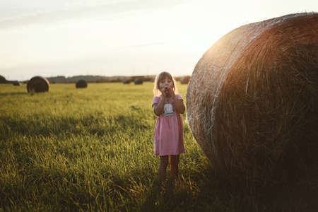 A happy child runs through a field of haystacks at sunsetの写真素材
