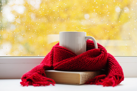 Autumn still life - Warm knitted scarf and cup of tea near a window, copy space.の写真素材