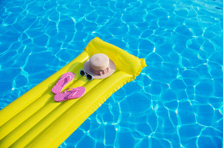 Beach summer holiday background. Inflatable air mattress, flip flops and hat on swimming pool.の写真素材
