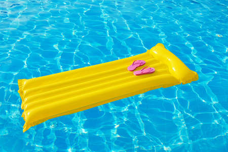 Beach summer holiday background. Inflatable air mattress, flip flops and hat on swimming pool.の写真素材